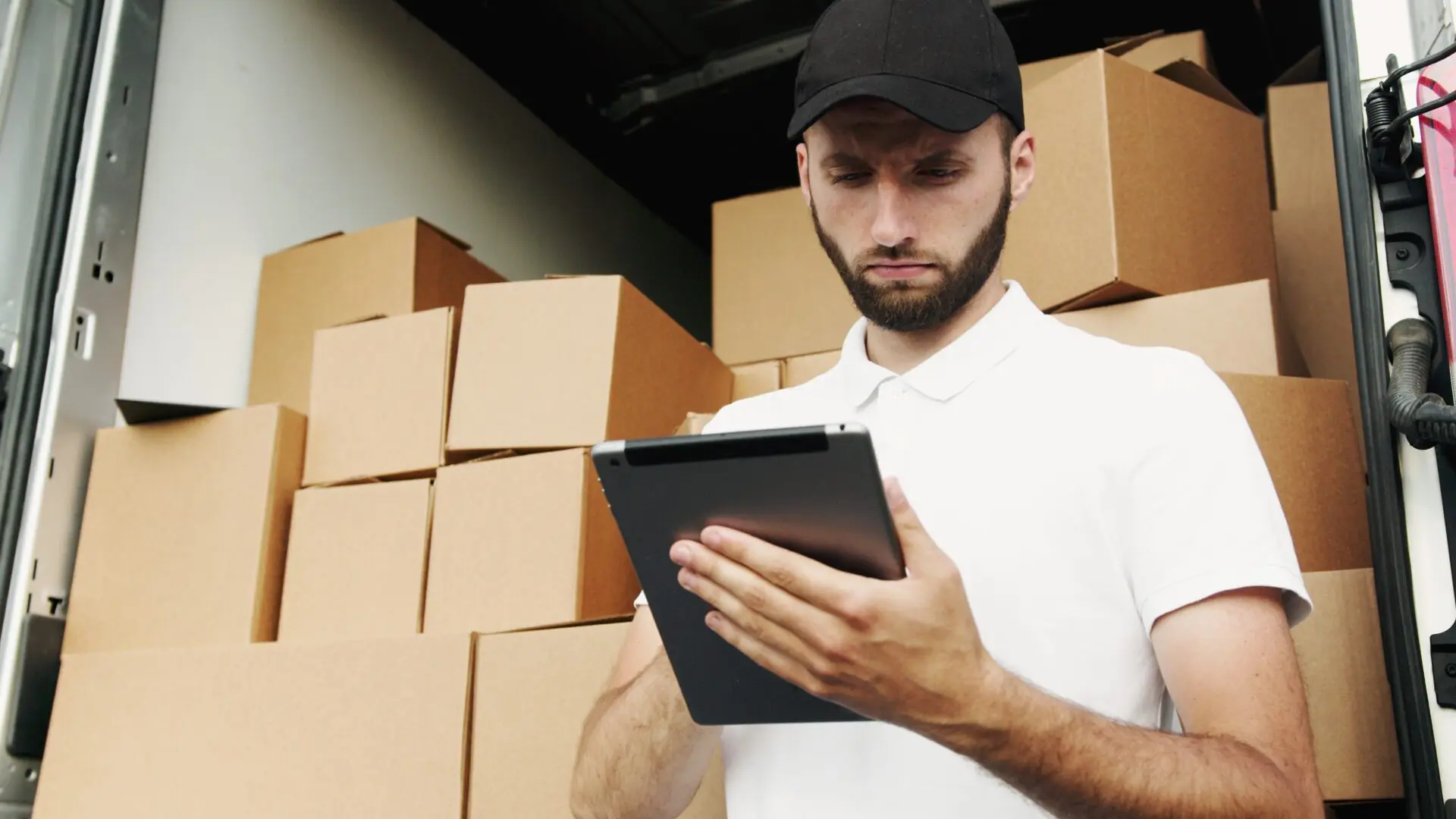 pexels-artem-podrez-5025643 A man holding a tablet in front of boxes.
