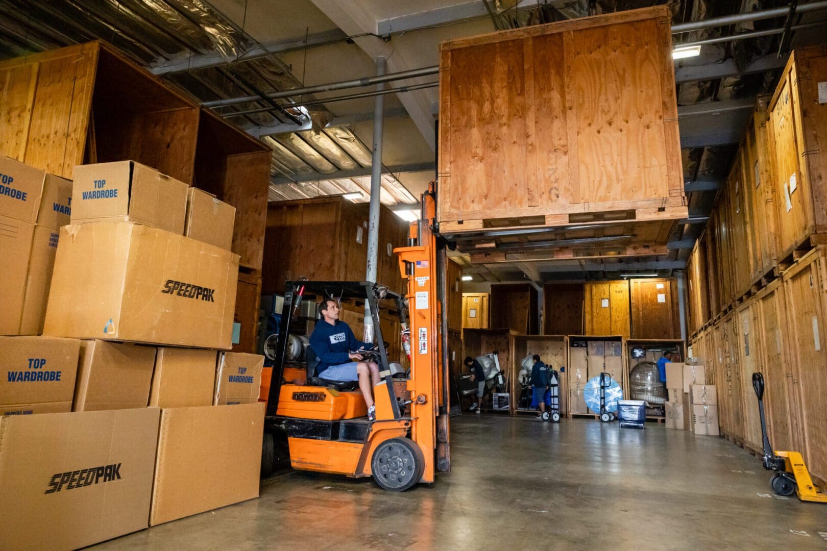 A man in an orange forklift driving through boxes.