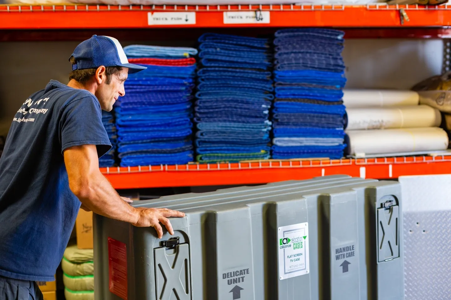 A man holding a large container in front of stacks of blue blankets.