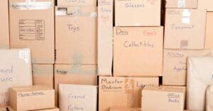 A stacked pile of cardboard moving boxes of various sizes and shapes that are taped shut and labeled with their contents.