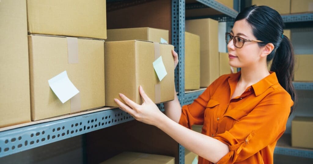 A woman in a professional storage room. Several cardboard boxes with labeled notes on them are on the shelves.