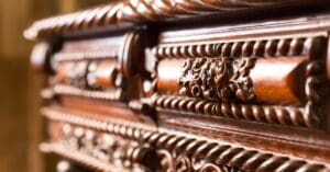 A sleek and brown antique wooden table has intricate carving on the side. The focus is on the carving over the blurred background.