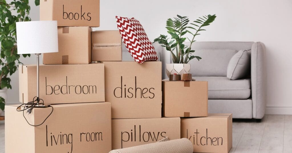 A stack of cardboard boxes in front of a living room couch. Some boxes have labels like "dishes" or "living room"