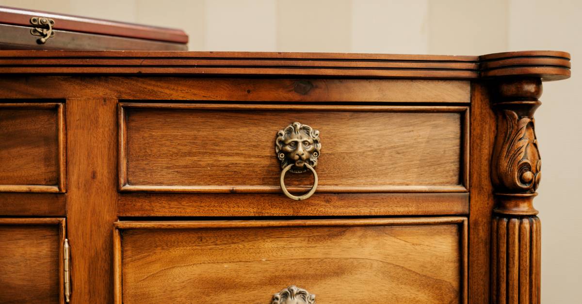 An ornate wooden chest with drawers and cabinets. The drawers have decorative metal lion head handles.